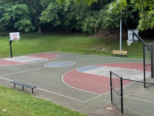 A basketball court is tucked along the tree-lined edge of the park
