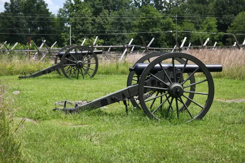 Two Civil War cannons positioned along a fence line on the open battlefield grounds