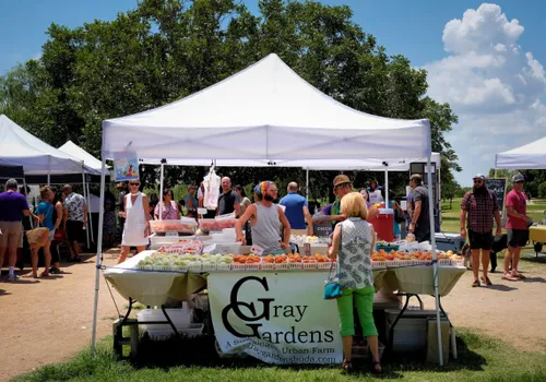 Bustling farmers market with vendors under white tents