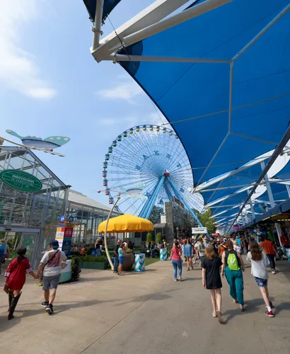 Visitors stroll through Fair Park with the Ferris wheel backdrop