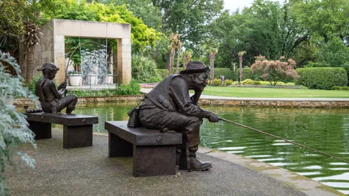 Bronze sculptures of seated figures fish in a garden pond