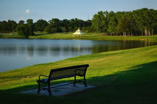 A park bench overlooks the calm lake with a pavilion visible in the background