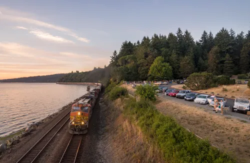 Freight train passing along the shoreline at sunset