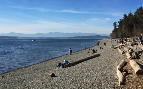 Visitors relax along the rocky shoreline with mountain views in the distance